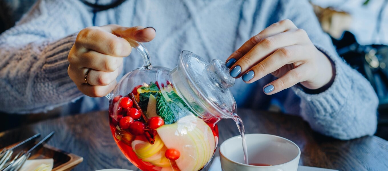 A woman with blue press-on nails pouring a tea pot to a cup.