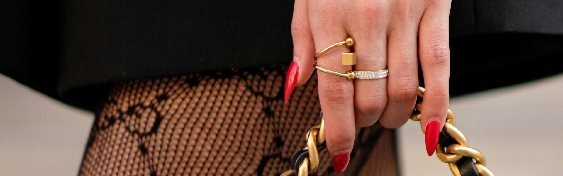 This is a decoration on contact page. A woman with a hand bag, The hand is holding a gold-colored chain bag. The woman's fingernails are a bright red.